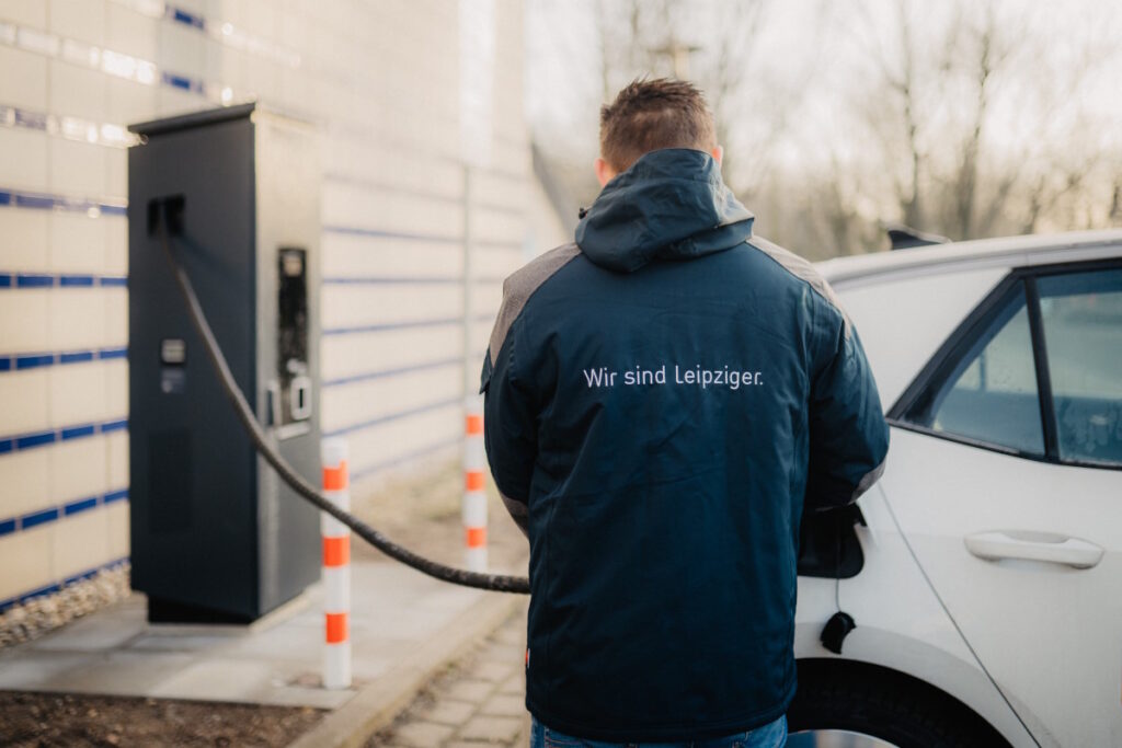 Ein Mann steht an seinem E-Auto und schließt dieses gerade an die Ladesäule an.